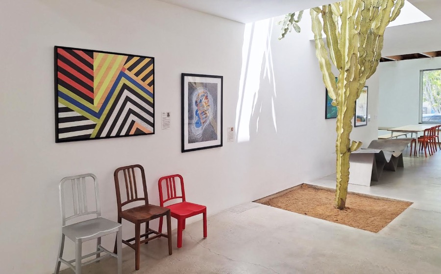 Large geometric painting anchoring a light-filled, plant-filled workspace