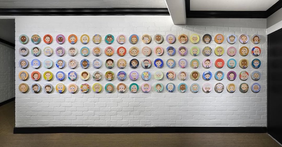 Wall installation of dozens of circular painted face portraits