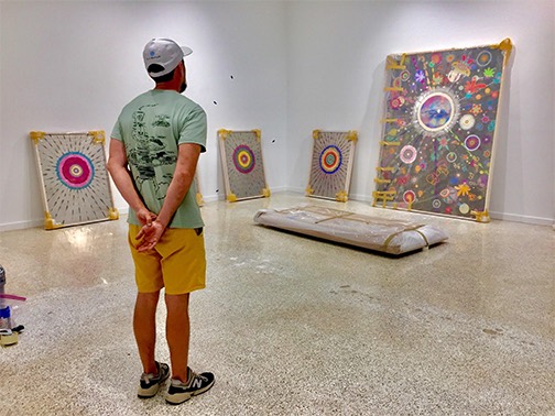 Visitor studying a group of mandala paintings propped against a gallery wall