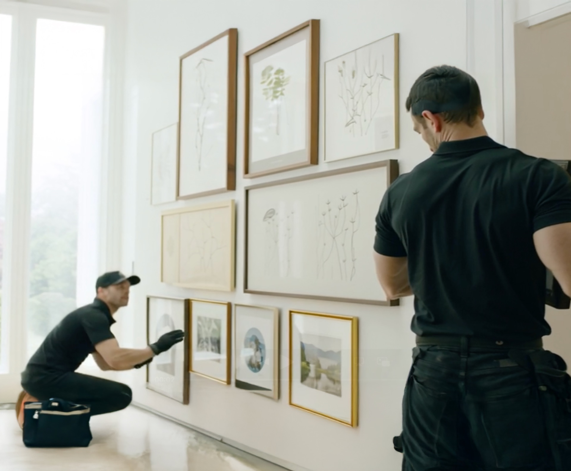 allART installers hanging a salon-style gallery wall of framed works in a bright residence