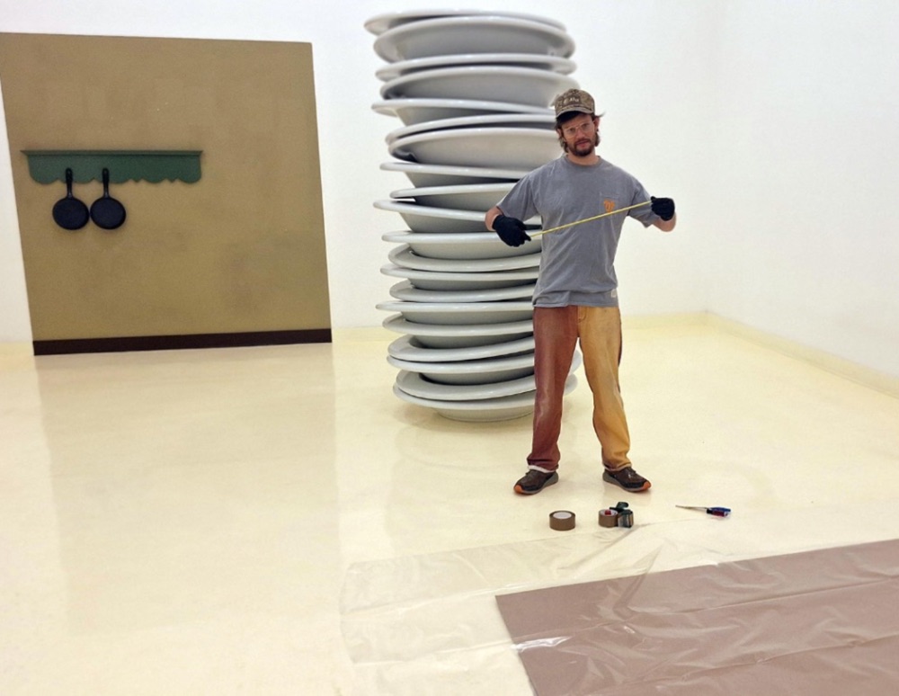 Art handler measuring a tall stacked-plate sculpture in a gallery